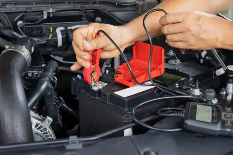Ręce podłączają prostownik do akumulatora, by sprawdzić, czy można odpalić auto z prostownika.