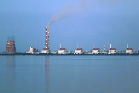 Zaporoże: potężna elektrownia atomowa z chłodnią kominową i dymiącymi kominami, na tle spokojnej wody.