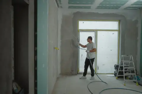 Pracownik nakłada gładź agregatem. Zastanawiasz się, ile kosztuje położenie gładzi? Sprawdź!