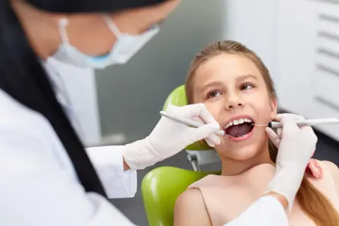 Dziecko u dentysty, które czeka na znieczulenie. Stomatolog w rękawiczkach bada ząb dziewczynki.