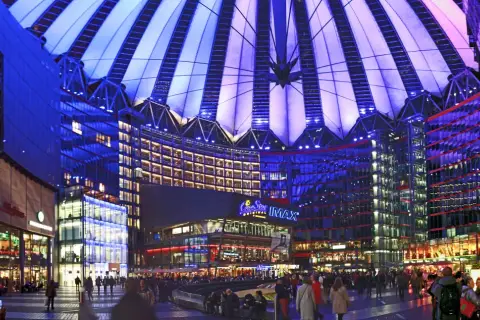Nocny widok na Sony Center w Berlinie, z oświetlonym dachem i fasadami budynków, pełen ludzi spacerujących po placu.