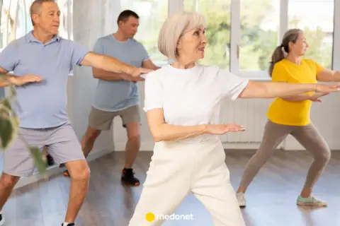 Seniorzy ćwiczą tai chi na krześle, synchronizując ruchy ramion.