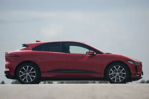 Czerwony jaguar elektryczny z profilu, z widocznymi felgami i linią dachu.