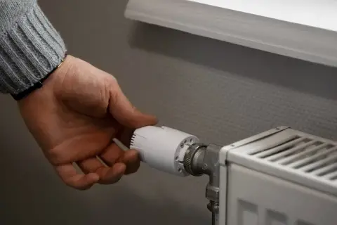 Dłoń reguluje termostat grzejnika, kontrolując, ile wynosi ogrzewanie gazowe.
