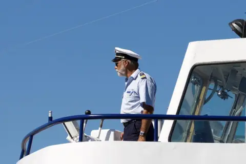 Kapitan na mostku statku, wpatrzony w dal. Zastanawia się, ile zarabia marynarz na jego stanowisku.