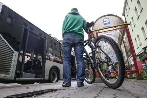 Mężczyzna z rowerem czeka na autobus. Rower stoi obok niego przy przystanku.