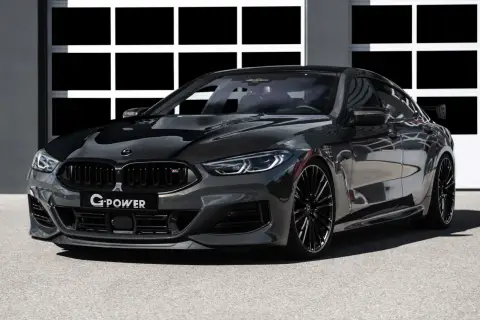 Ein getunter BMW M850 Gran Coupé in dunklem Grau mit Carbon-Elementen und auffälligem Heckspoiler steht vor einer Garage.