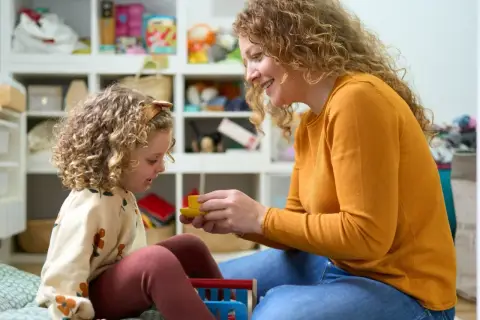 Mama z córką bawią się w pokoju pełnym zabawek. Czy urlop wychowawczy wlicza się do stażu pracy? To pytanie nurtuje wiele mam.