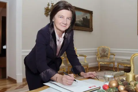 Małgorzata Łaszcz, w eleganckim stroju, pochyla się nad dokumentami. Jej życiorys jest bogaty w doświadczenia.