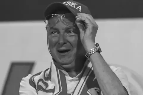 Uśmiechnięty mężczyzna w czapce z daszkiem i okularach, z szalikiem na szyi. To może być nicola zalewski tata, dumny z syna.