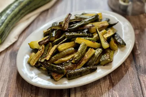 Zucchine al forno con pangrattato e parmigiano, dorate e croccanti, servite su un piatto bianco.