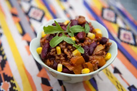 Miseczka pełna aromatycznego chili con carne przepis oryginalny, z fasolą, kukurydzą i mięsem mielonym, ozdobiona świeżymi ziołami.