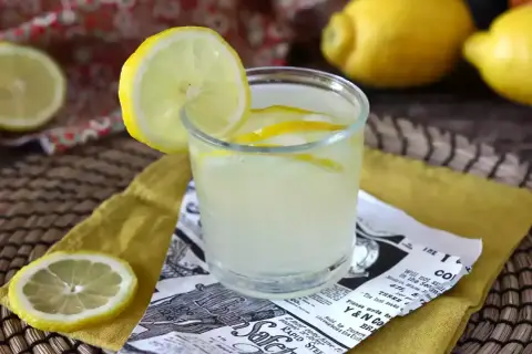 Orzeźwiający drink z limoncello, ozdobiony plasterkiem cytryny, na tle cytryn i wzorzystej tkaniny.