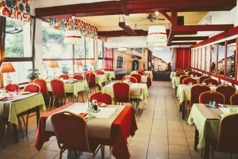 Wnętrze restauracji z czerwonymi krzesłami i stolikami nakrytymi na przyjęcie. Mural z ulicą przypomina czardasz Gdańsk.