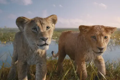 Dwa lwiątka, Simba i Nala, w realistycznej wersji Króla Lwa, stoją na tle sawanny i wody.