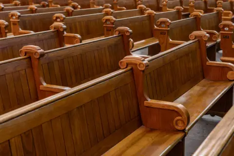 Puste, drewniane ławki w kościele, symbolizujące rezygnację z religii i pustkę po odejściu wiary.