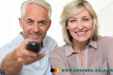 Glückliches Rentnerpaar mit Fernbedienung. Informieren Sie sich über die GEZ-Befreiung für Rentner und die Einkommensgrenze auf www.buerger-geld.org.