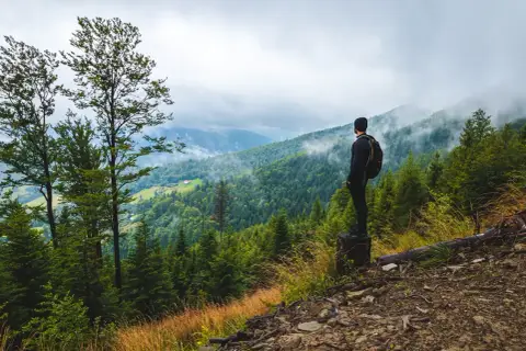 Mężczyzna z plecakiem podziwia widok na górzyste tereny podczas **hiking po polsku**. Mgła spowija szczyty, tworząc malowniczy krajobraz.