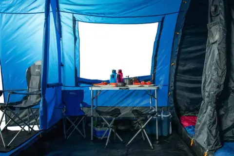 Wnętrze niebieskiego namiotu z rozstawionym stołem, krzesłami i śpiworami. Doskonała wodoodporność namiotu zapewnia komfortowe warunki.