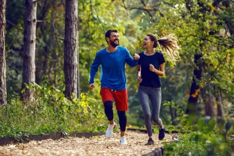 Szczęśliwa para cieszy się wspólnym trail run w jesiennym lesie.