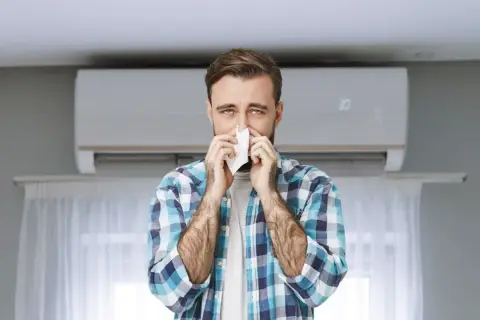Hombre con pañuelo en la nariz, con aire acondicionado de fondo. Podría ser que se puede tener alergia al aire acondicionado.