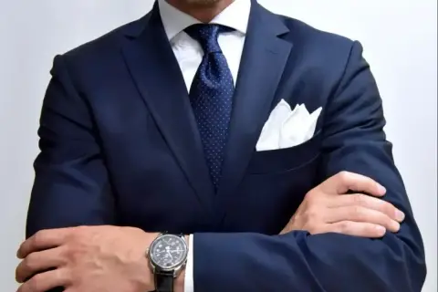 Elegancki mężczyzna w granatowym garniturze, białej koszuli i granatowym krawacie w kropki. Idealna inspiracja, jaki krawat do granatowej koszuli.