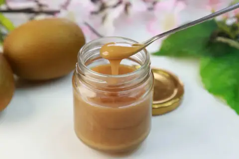Gęsty, złocisty miód manuka na łyżeczce, obok owoców kiwi. Odkryj niezwykłe miód manuka właściwości.