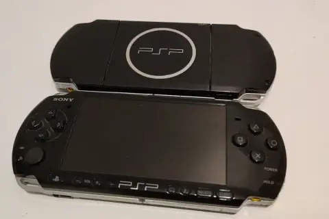 Dwa czarne modele przenośnej konsoli Sony PSP, jeden na drugim. Górny model z logo PSP i napisem UMD. Dolny model z ekranem, przyciskami i analogiem. Nowe psp gotowe do gry.