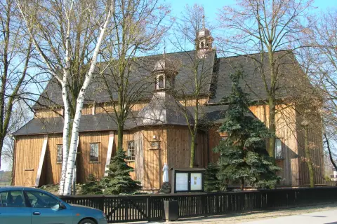 Drewniany kościół w Beniowej, otoczony drzewami, z charakterystyczną wieżyczką i ogrodzeniem.