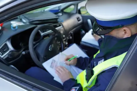 Policjant w radiowozie spisuje mandat za jazdę bez kasku.