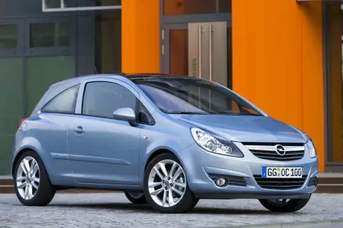 Niebieski Opel Corsa D 1.2 benzyna stoi przed pomarańczowym budynkiem.