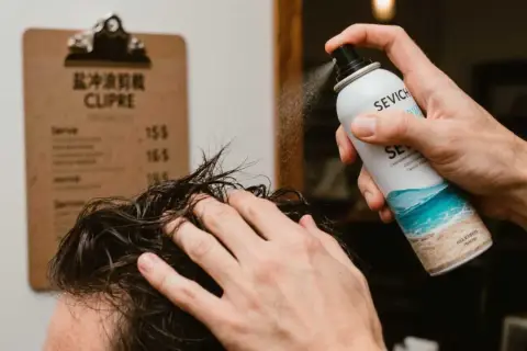 Un hombre aplica spray sal marina pelo para un look playero.