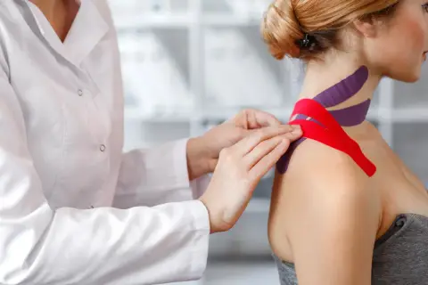 Fizjoterapeuta zakłada taśmy na szyję pacjentki. Warto znać kinesiotaping przeciwwskazania, by uniknąć problemów.
