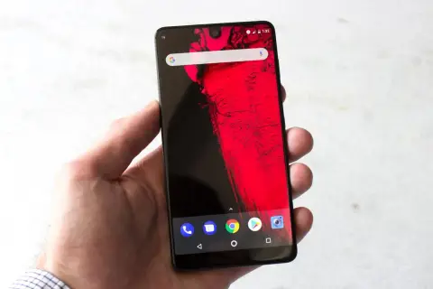 Dłoń trzyma smartfon z wycięciem (notch) na górze ekranu, wyświetlający czerwony wzór i ikonki Androida.