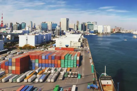Kontenery czekają na załadunek. Ta wielka paczka do Japonii popłynie statkiem przez ocean, mijając nowoczesne miasto.