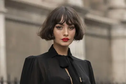 Mujer con un elegante corte de pelo **french bob**, labios rojos vibrantes y un top negro con lazada.