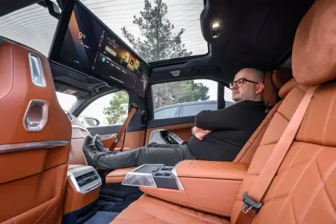 Wnętrze BMW i6 z ekranem multimedialnym dla pasażerów. Mężczyzna relaksuje się na tylnym siedzeniu.