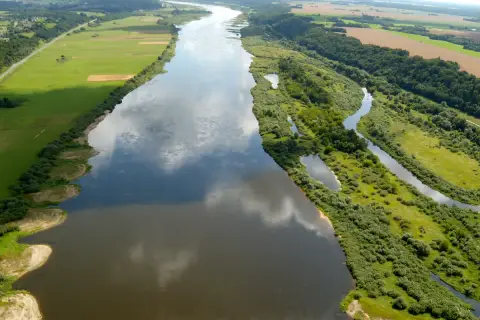 Szeroka rzeka Nemen meandruje przez zielone pola i lasy, odbijając chmury na swojej tafli.