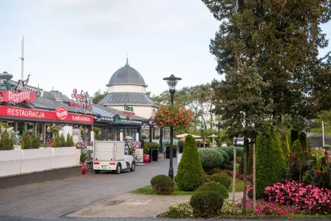 Spacer po alei gwiazd w Międzyzdrojach, z restauracjami i kawiarniami po lewej stronie, a zielenią i drzewami po prawej.