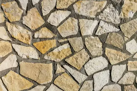 Kamienna ściana z nieregularnych, żółtawych i białych kamieni. Piaskowiec tworzy naturalną, rustykalną mozaikę.