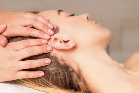 Mains douces appliquant une thérapie cranio sacrée sur la tête d'une femme détendue.