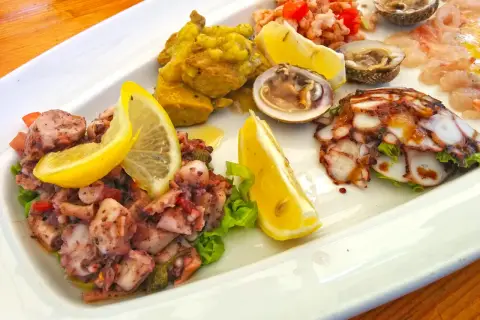 Pyszne dania chorwackie: sałatka z ośmiornicy, krewetki, małże i carpaccio z ryby, ozdobione cytryną.