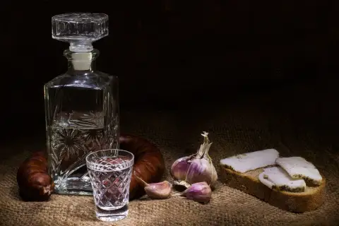 Wódka smakowa w karafce i kieliszku, obok kiełbasa, czosnek i chleb ze smalcem. Widoczne objawy utlenienia wódki smakowej po długim staniu w słońcu.