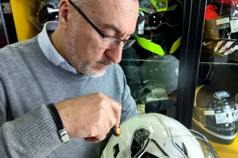 Uomo con cacciavite regola la visiera di un casco bianco, assicurandosi che il casco debba avere la visiera priva di graffi.