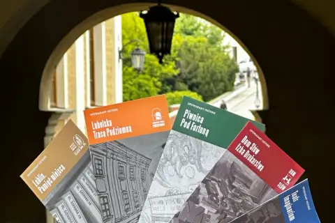 Książki o historii Lublina, m.in. "Lubelska Trasa Podziemna" i "Piwnica Pod Fortuną", prezentowane na tle bramy. Teatr NN Lublin zaprasza do odkrywania przeszłości.