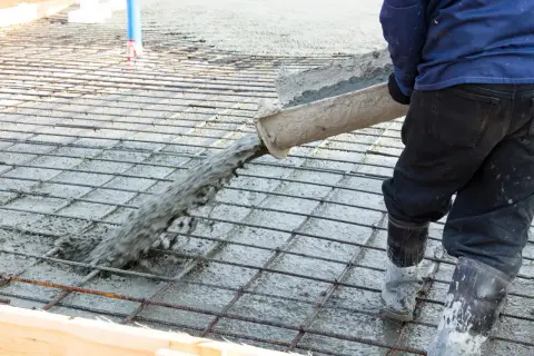 Betoniarz wylewa beton na zbrojenie, które zawiera włókna polipropylenowe, tworząc solidną posadzkę.
