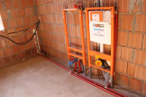 Instalacja hydrauliczna przed tynkami: stelaże podtynkowe, rury i spłuczka JomoTech w budowie.