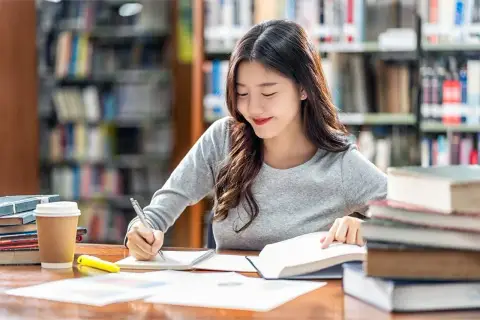 Młoda kobieta studiuje w bibliotece, otoczona książkami. Jej skupienie i lekki uśmiech sugerują, że pokonuje wszelki sceptycyzm w drodze do wiedzy.
