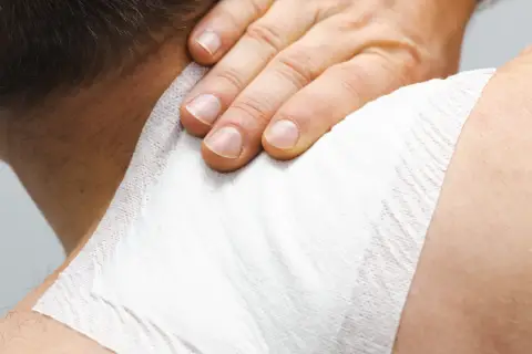 Dłoń uciska plaster przeciwbólowy na karku, przynosząc ulgę w bólu.