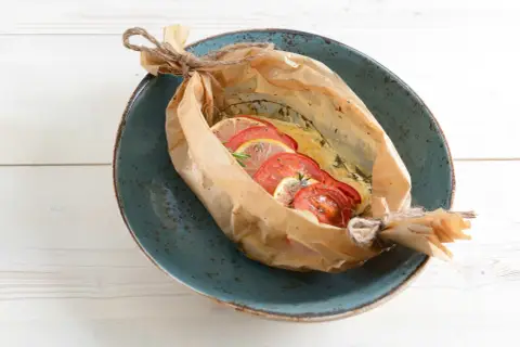 Bar au barbecue en papillote, garni de rondelles de tomates et de citron, prêt à être dégusté.